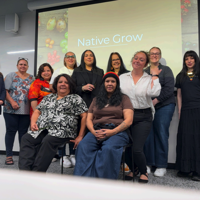A group of women posing together in front of a "Native Grow" presentation slide in a meeting room.